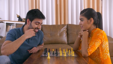 Modern Indian couple playing board game at home - Playing Chess. Indian stock video of Indian woman defeating her husband in the game of chess. Healthy and happy family playing competitive chess