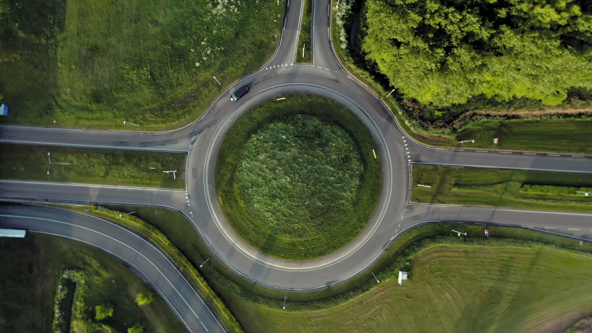 Top-down aerial view of a green roundabout with camera rotating and following moving cars Royalty-Free Stock Footage #1029646925