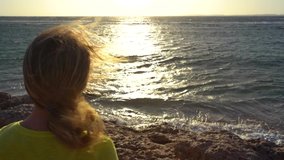 Closeup back view of white blond caucasian woman standing at seashore during sunrise time. Windy morning. Slow motion full hd video footage.