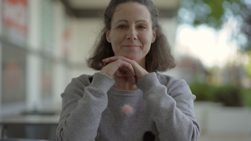 Happy mature woman looking at camera. Smiling middle aged brunette with hands on chin posing outdoor. Happiness concept