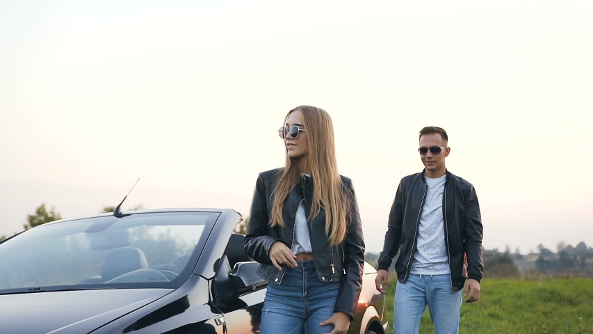Happy young man hugging young attractive woman standing near the car, cabriolet on the field background.