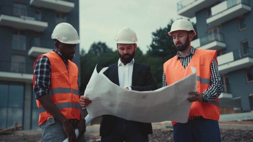 Handsome businessman inspects the project along with multiracial construction team in protective helmets and signal jackets, they shake their hands. Agreement, success. | Shutterstock HD Video #1029681344
