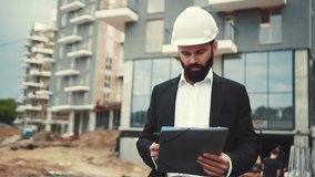 Handsome bearded man in formal stylish black suit and hard hat holds the documents folder, walks down the construction site and actively communicates via phone. Profession concept. - Powered by Shutterstock - Get 15% off with code: PIKWIZARD15