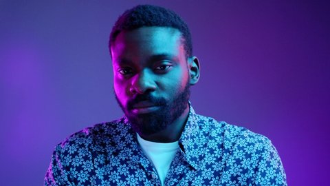 Portrait of handsome young African American male dressed in flowered shirt looking at camera with serious and confident expression on his face in neon lights. People and lifestyle concept. Male studio