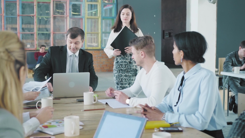 A businessman and a hired manager enter the office and go to the table where their colleagues are waiting for them. They greet the staff and start meet up. Creative office interior. Coworking team | Shutterstock HD Video #1029684650
