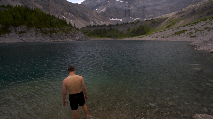 Wide shot of athletic man diving into lake. Shot ends with him swimming to the surface.