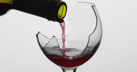 Wine. Red wine pouring in broken wine glass on the white background. Rose wine pour from the bottle. Close up shot