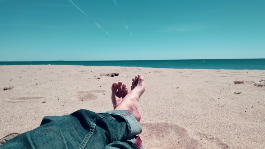 Vacation holidays. Man feet closeup relxing on beach on sunbed enjoying sun on sunny summer day. Legs with jeans