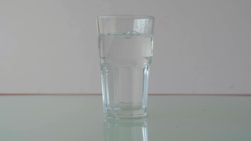 Pouring water in glass on table with relfection, still close-up shot in minimalist setup