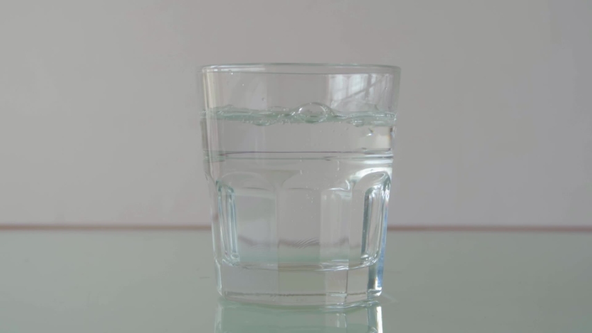 Pouring water in glass on table with relfection, still extreme close-up shot in minimalist setup
