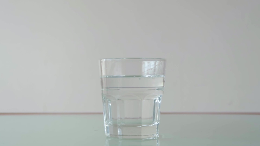 Pouring water in short glass on table with relfection, still close-up shot in minimalist setup