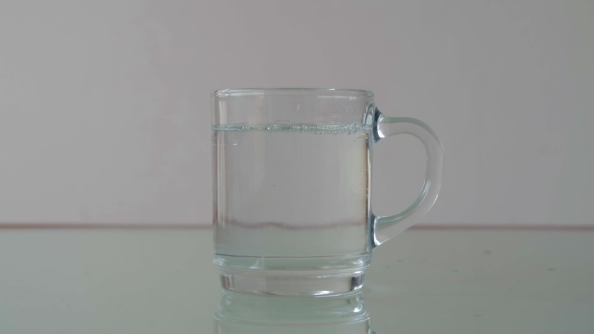 Pouring water in glass cup on table with relfection, still close-up shot in minimalist setup