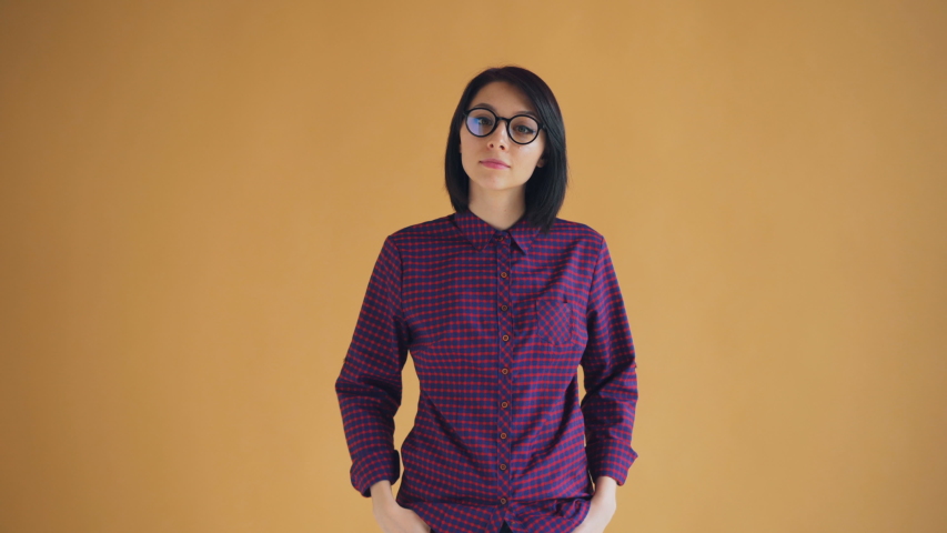 Portrait of happy girl with black hair showing thumbs-up smiling recommending standing against orange nackground. Young people and positivity concept.