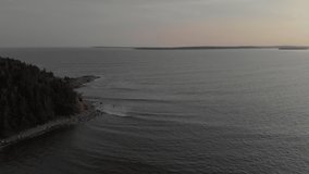 Cinematic drone / aerial footage rotating showing some hills and a forest by the sea in Kingsburg, Nova Scotia, Canada during summer season - sunset time.