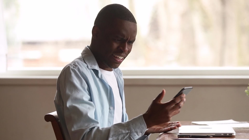 Mad stressed african man holding cellphone annoyed with mobile app error spam message on slow stuck broken smartphone, angry black guy frustrated by phone problem having complaints on bad service | Shutterstock HD Video #1029713885