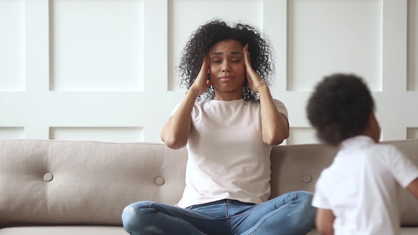 Stressed upset african american mom feeling migraine headache tired of too active kids running around, annoyed single black mother desperate about two difficult naughty children misbehaving at home  Royalty-Free Stock Footage #1029713954