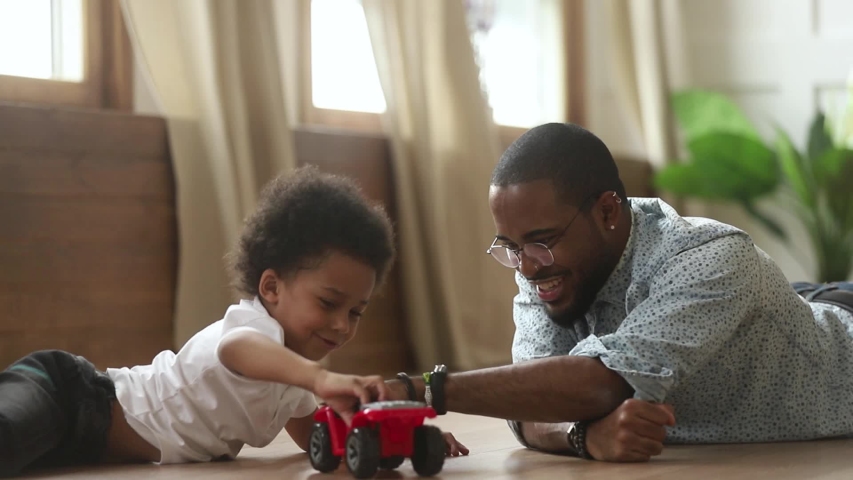 Happy african american cute little son playing toy cars with loving young dad babysitter, funny small kid son and black father having fun racing on warm floor at home, family daddy child men games Royalty-Free Stock Footage #1029713981