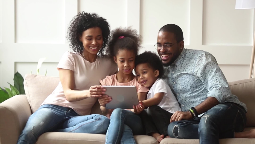 Cute little african children play online game using digital tablet having fun with parental control sit on sofa, happy black family laugh look at computer screen together enjoy do internet shopping Royalty-Free Stock Footage #1029714005