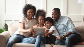 Cute little african children play online game using digital tablet having fun with parental control sit on sofa, happy black family laugh look at computer screen together enjoy do internet shopping