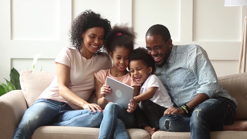 Cute little african children play online game using digital tablet having fun with parental control sit on sofa, happy black family laugh look at computer screen together enjoy do internet shopping Royalty-Free Stock Footage #1029714005