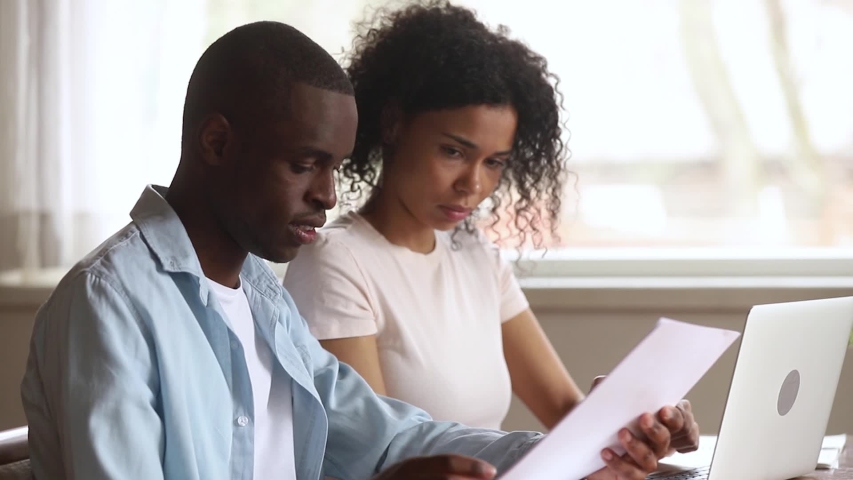 Serious african american couple talking doing paperwork using laptop together, focused family calculate pay bill rental payment online on computer holding paper at home office, mentor teaching intern Royalty-Free Stock Footage #1029714071