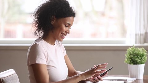 Smiling african american woman using smartphone dating app looking swiping on screen, happy mixed race young girl holding phone enjoy watching media in mobile online application on cellphone