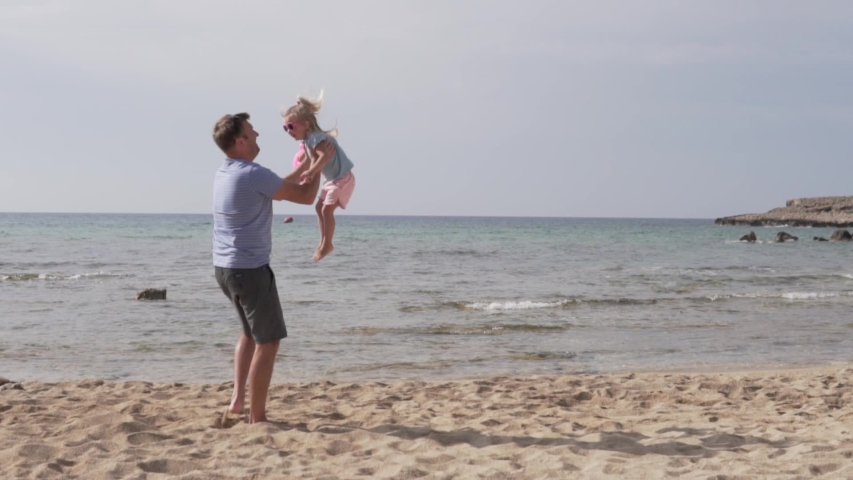 Slow motion of handsome father throwing his adorable daughter in the air. Dad plays with his daughter on the beach by the sea, a man throws up the baby in the top