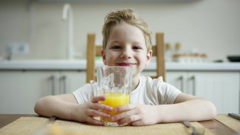 cute boy sitting at the table with glass of orange juice and waiting for a other family to have a meal overrun camera