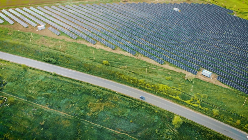 Aerial view of powerful station with solar panels generates electric current with help of sunlight is located in field near road on which pass cars. Drone shoots video of energy saving