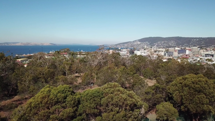 Aerial pan up over trees to reveal seaside port and city of Hobart, Tasmania, Australia