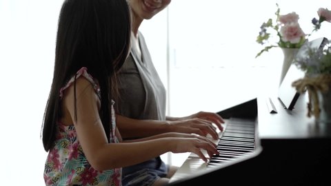 Slow motion footage of Asian mother and her daughter playing piano together. Mother teaching daughter with happiness and smile while they pressing the piano key. Happy family activities concept.