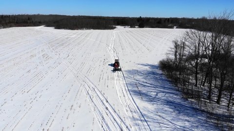Aerial, drone shot, following a tractor and a trailer, driving on a snowy field, on a cold, winter day, in Ottawa Valley, Ontario, Canada