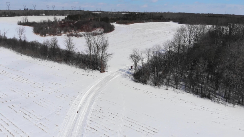 Aerial, rising, drone shot, of a woman cross country skiing, on a snowy field, on a cold, winter day, in Ottawa Valley, Ontario, Canada