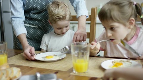 mother cut the scruble eggs for son during the family dinner
