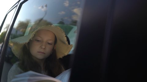 Girl with straw hat Reading Book Inside Car in backseat. road trip concept