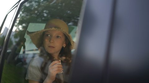 little pretty girl with straw hat eating chocolate in car backseat. road trip concept.