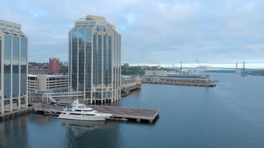 Cinematic drone / aerial footage rotating showing waterfront docks and buildings, the port and a bridge in Halifax, Nova Scotia, Canada during summer season.