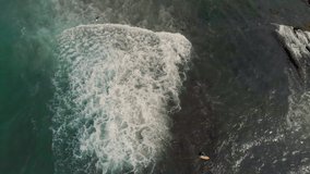 Cinematic drone / aerial static footage showing two surfers from above while waves push them during summer season.