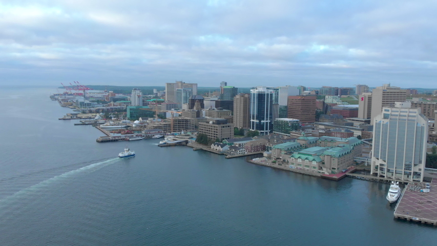 Cinematic drone / aerial footage rotating showing waterfront docks and buildings, the port and sighseeing ships in Halifax, Nova Scotia, Canada during summer season.