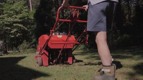 Man using gas powered aerating machine to aerate residential grass yard. Lawn aeration being performed by groundskeeper using powered landscaping equipment.
