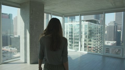 Woman walking into a new apartment with outstanding city view of Los Angeles Downtown.  Empty apartment with glass walls. floor to ceiling windows