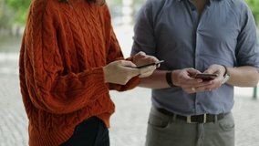 Cropped shot of people using smartphones outdoor. Mid section of man and woman standing together on street and using mobile phones. Technology concept