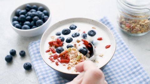 Yogurt bowl with berries and granola for breakfast. Taking spoonful of yogurt with blueberries, goji and crunchy granola. Healthy eating concept