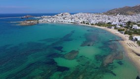 Aerial drone panoramic video of famous turquoise sea sandy beach of Saint George next to chora main town of Naxos island with beautiful uphill castle, Cyclades, Greece