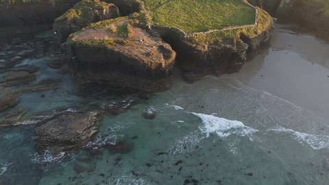 Aerial: Playa de las Catedrales Galicia Spain at Sunset. Beach of spectacular cliffs and cracks facing Atlantic ocean. Popular touristic place