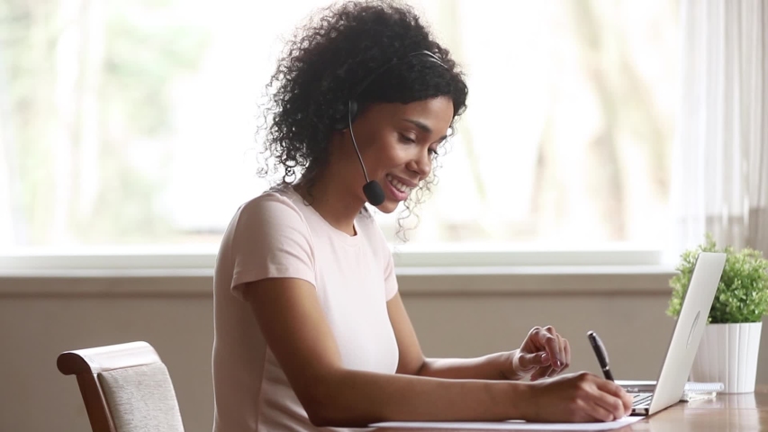 Young woman african american female  teacher wearing wireless headset talking looking at laptop teaching student making conference video call e tutoring lesson learning in internet write notes Royalty-Free Stock Footage #1029780932