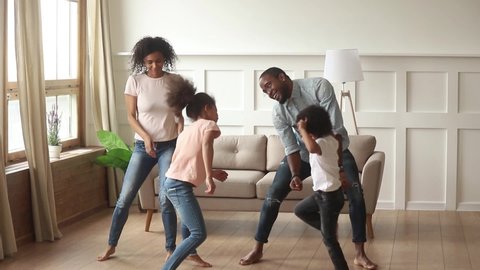 Carefree active black parents and small cute kids dancing together in living room, happy african family mom dad with little funny kids laughing having fun jumping enjoying leisure weekend activity 