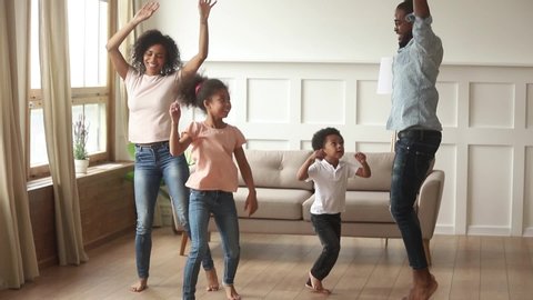 Happy african american parents and cute funny kids dancing laughing in living room, black mom dad with little children enjoying jumping having fun together, family of four funny leisure activity