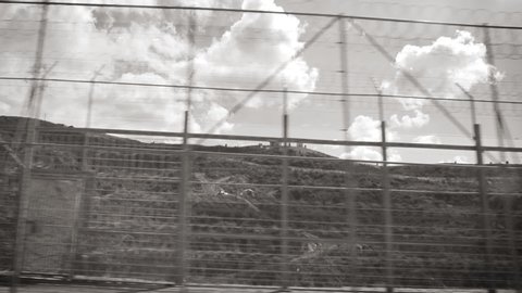 Ceuta, Spain Black and white - Footage of double barbed wire fence at Moroccan border in difficult terrain built to stop migrant inflows into EU, pushback action at border as seen from vehicle driving