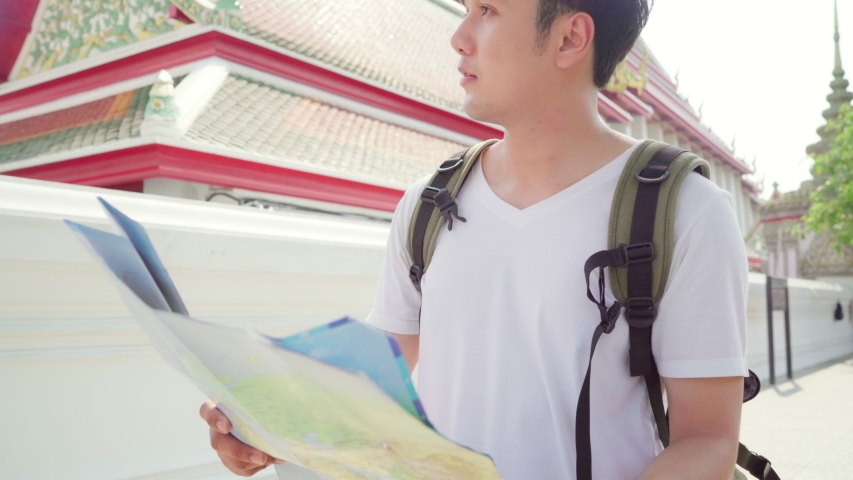 Traveler Asian man direction on location map in Bangkok, Thailand, backpacker male looking on map find landmark while spending holiday trip. Lifestyle men travel in Asia city concept.